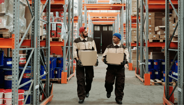 Two warehouse workers carrying boxes through a storage facility, representing agency workers impacted by the new Employment Rights Bill.
