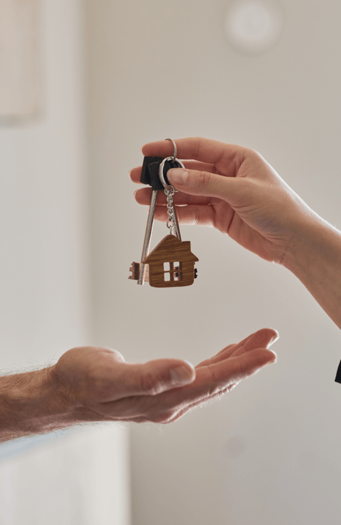 A hand gives a set of house-shaped keys to another open hand, symbolising a housing procurement.