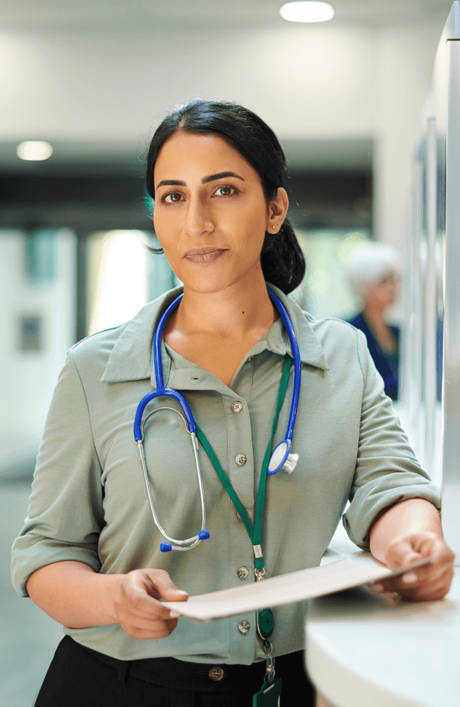 A healthcare professional with a stethoscope around her neck holds a clipboard in a hospital setting, representing healthcare procurement.