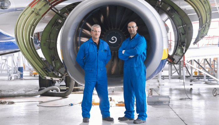 Two male engineers standing in front of a jet engine in blue overalls, representing transforming BPSS screening for Quest Global's engineering workforce by Security Watchdog