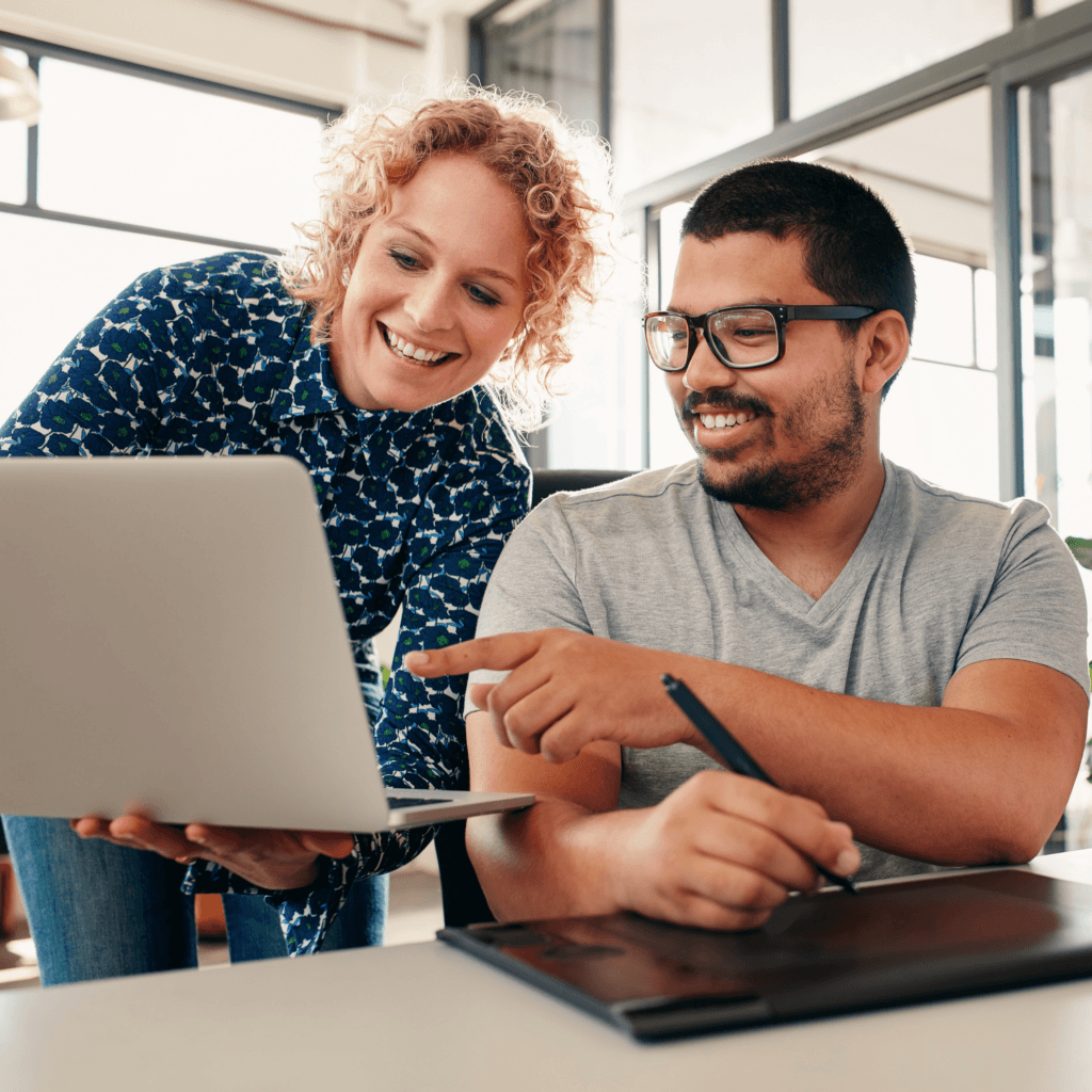 Two colleagues smiling while collaborating on a laptop in a bright office setting, symbolising successful procurement partnership with Matrix Milestone.