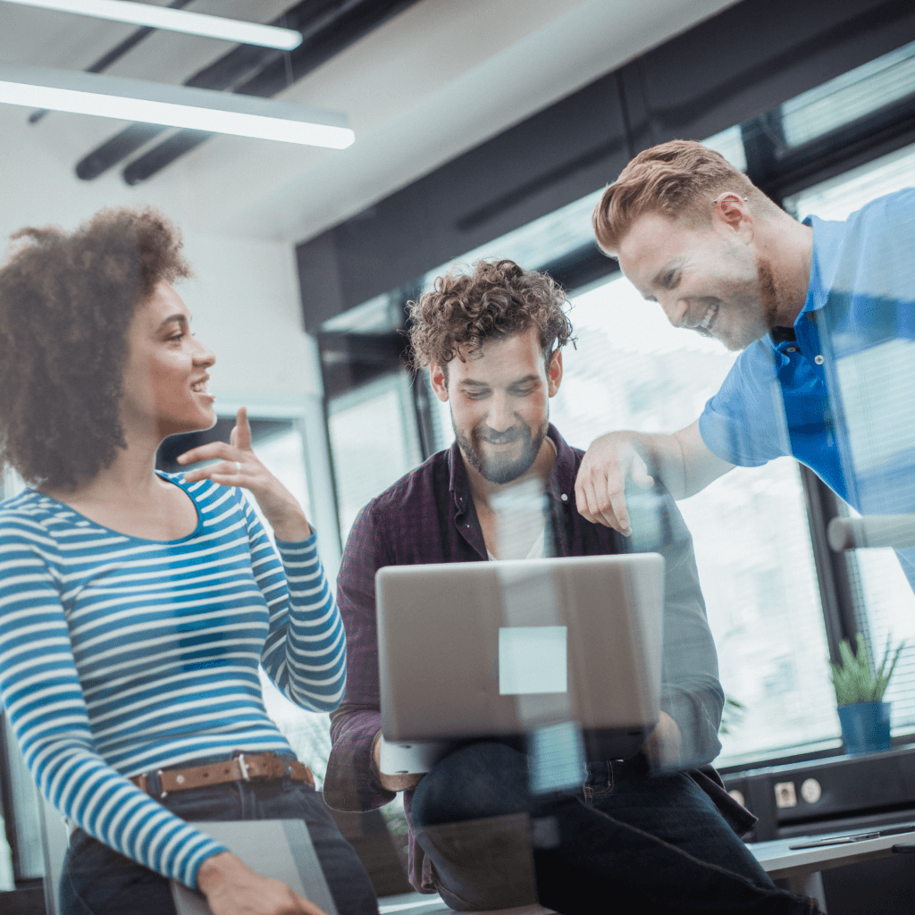 Three people smiling and collaborating around a laptop in a modern office setting, representing procurement partnership with matrix milestone.
