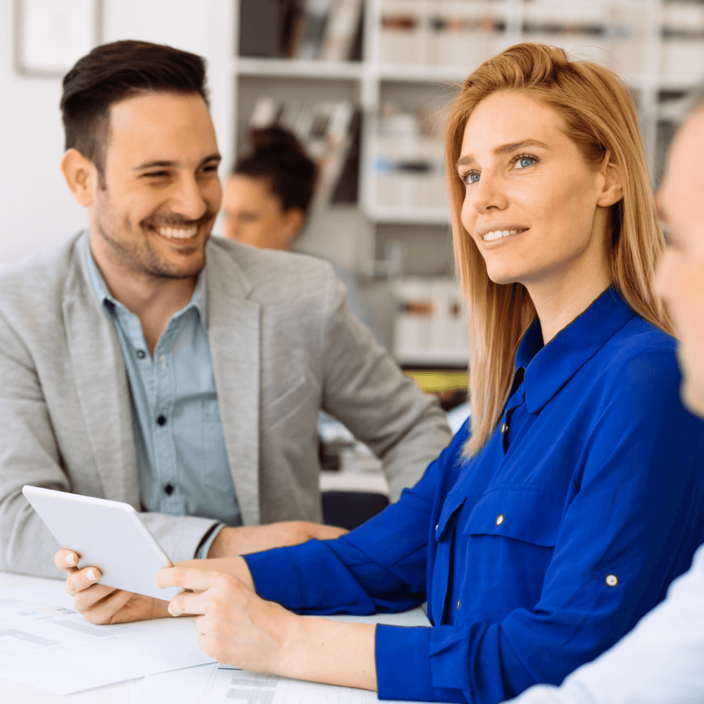 Three people in a meeting, one woman holding a tablet, seated around a table in a bright office setting, representing procurement management technology.