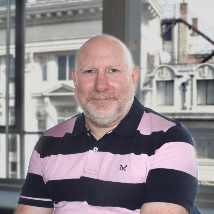 Workforce Management Experts - Andy Simms, Head of Supplier Management for Matrix, with beard in a pink and black striped shirt sits in front of a large window overlooking urban buildings.