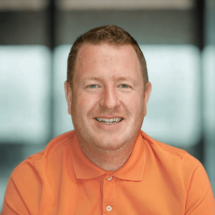 Workforce Management Experts - Chris Grimes, Sales Director of Matrix Workforce smiling, wearing an orange shirt, with a blurred background.