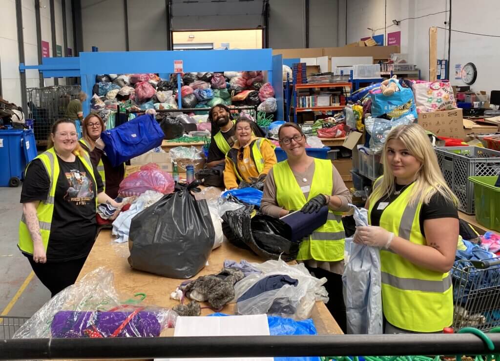 Group of people in high-visibility vests sorting donations in a warehouse setting.