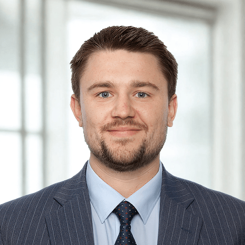 Jacob Mallett, Matrix CFO, with short brown hair and a beard is wearing a blue suit and tie, standing in front of a window.