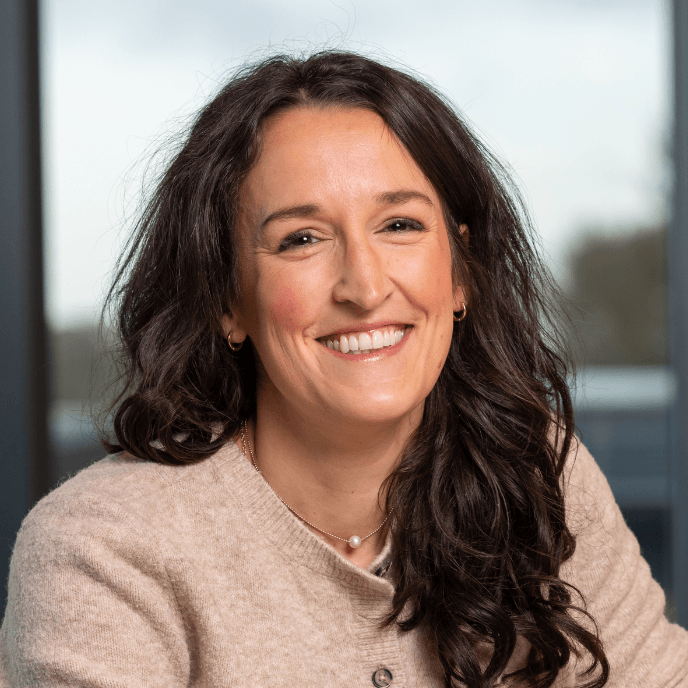 Jodie Ratcliffe, Chief People Officer at Matrix, smiling with long dark hair wearing a beige sweater, indoors with a blurred background.