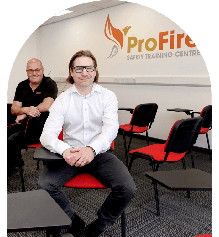 Two men seated in a training room with "ProFire Safety Training Centre" on the wall.