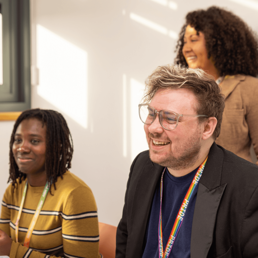 Three team Matrix colleagues smiling and sitting in a well-lit room, wearing lanyards, engaged in a discussion or workshop.