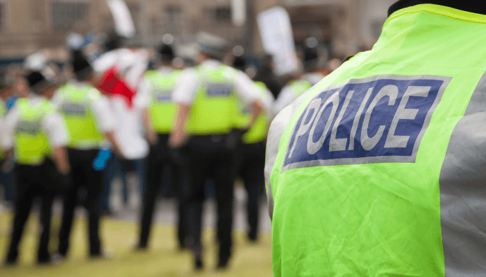 Police officer in a high-visibility jacket at a public event, with other officers in the background, representing the blue light environment where 7 Forces uses outcome-based procurement.