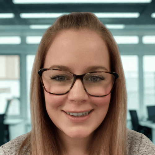 Person with long hair and glasses smiling in an office setting.